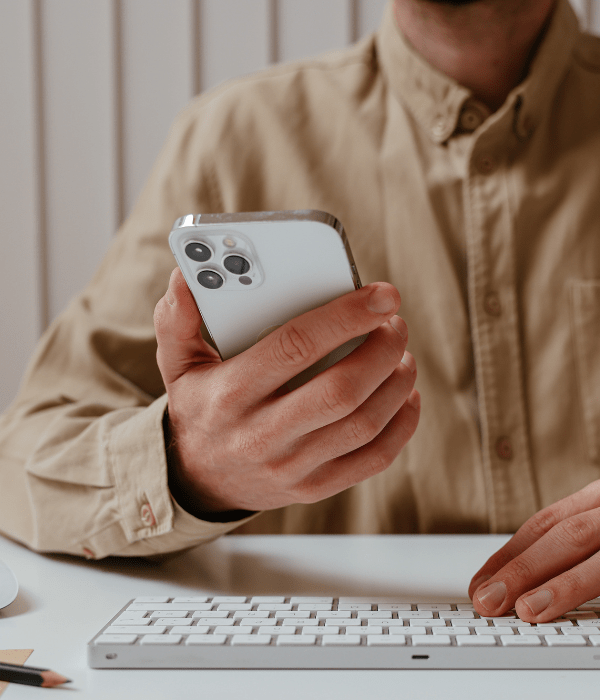 Persona de camisa beige sostiene celular con la otra mano sobre un teclado